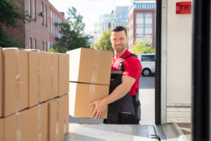 Portrait Of A Smiling Mover In Uniform Loading A Cardboard Boxes